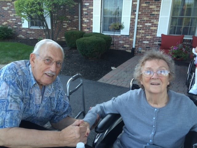 An elderly couple enjoying time outdoors in front of a brick building.
