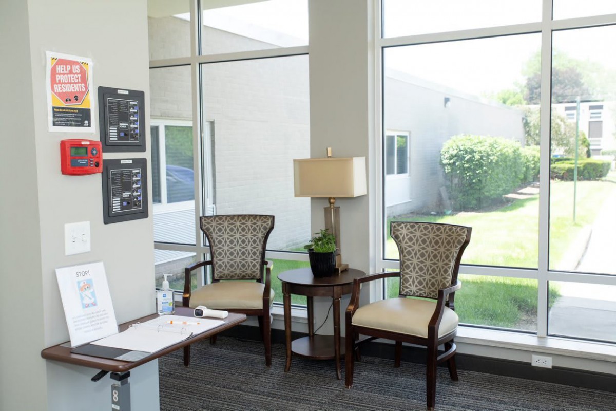 A bright waiting area with two chairs, a table, and a lamp beside large windows.