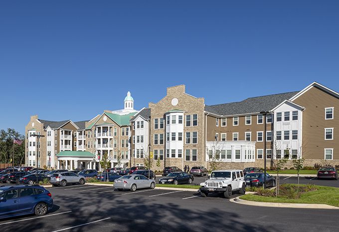A multi-story residential complex with a large parking area on a clear, sunny day.
