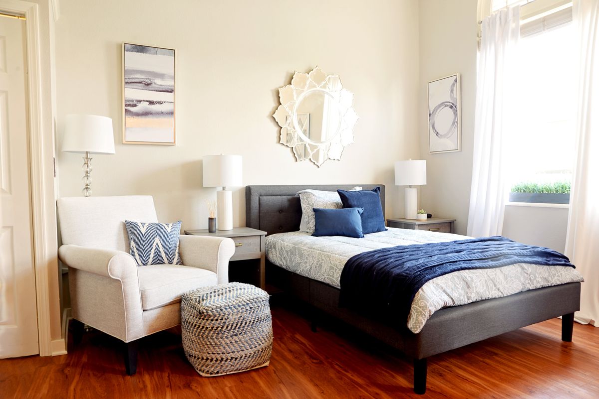 A cozy and stylish bedroom featuring a large bed with blue accents, an inviting armchair, decorative mirrors, and elegant lighting.