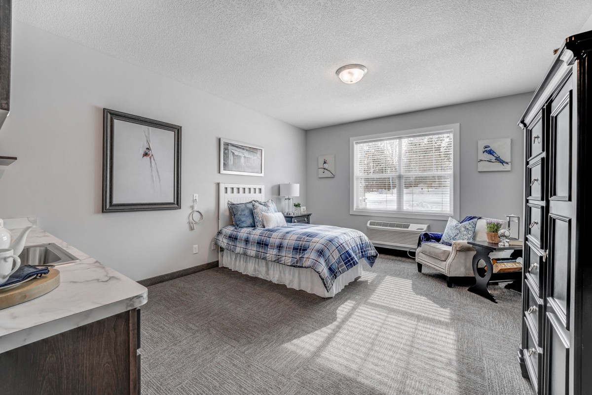 A cozy bedroom with a single bed, featuring blue bedding and ample natural light from a large window.