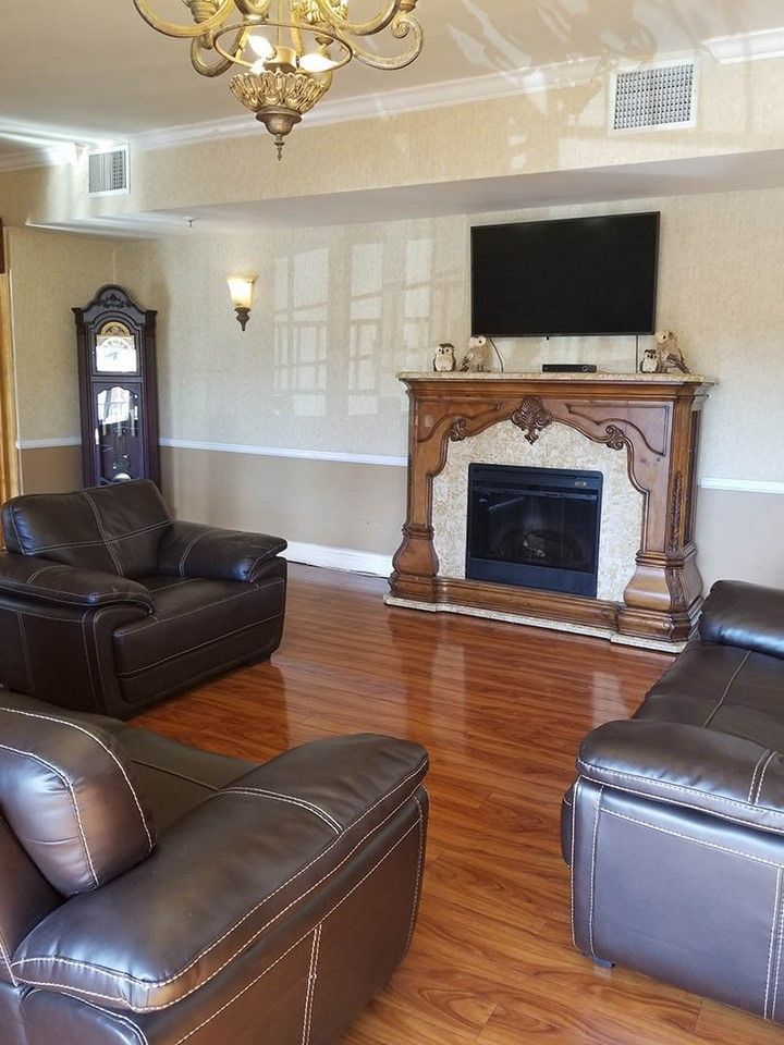 A traditional living room featuring leather chairs, a wooden fireplace, and a mounted television.