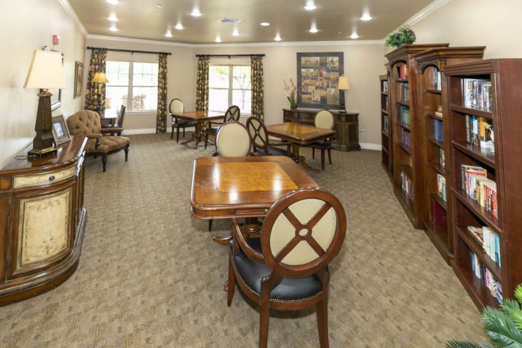 A cozy library room with wooden tables, comfortable chairs, and bookshelves filled with books.