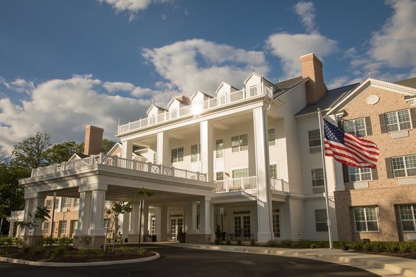Elegant colonial-style building with white pillars and flags against a backdrop of a partly cloudy sky.