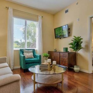 A cozy living room with a large window, featuring an armchair, sofa, coffee table, and television.