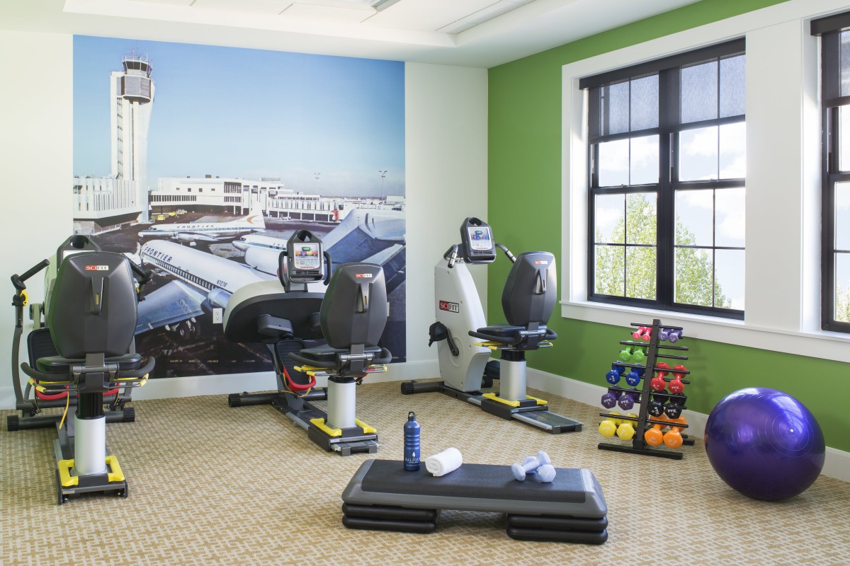 A well-equipped gym room featuring recumbent bikes, weights, and a step platform against a backdrop of cityscape wallpaper.