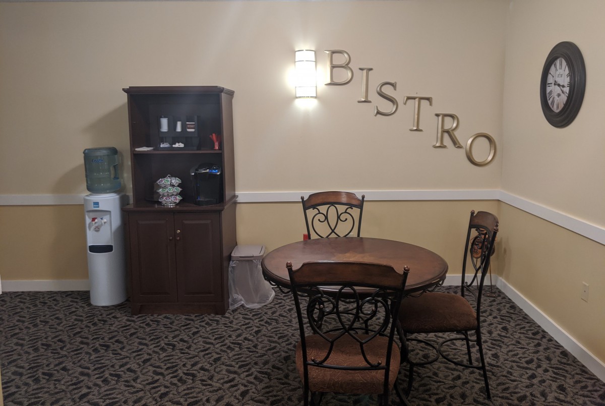 A cozy bistro corner with a table, chairs, and a cabinet with a water dispenser.
