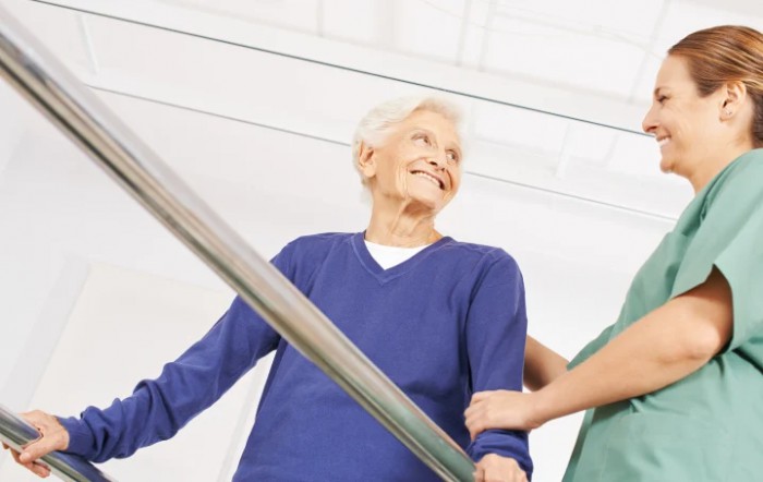 An elderly person receiving assistance while walking down a corridor.