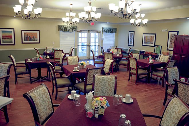 A well-lit dining room with neatly arranged tables and chairs in a formal setting.