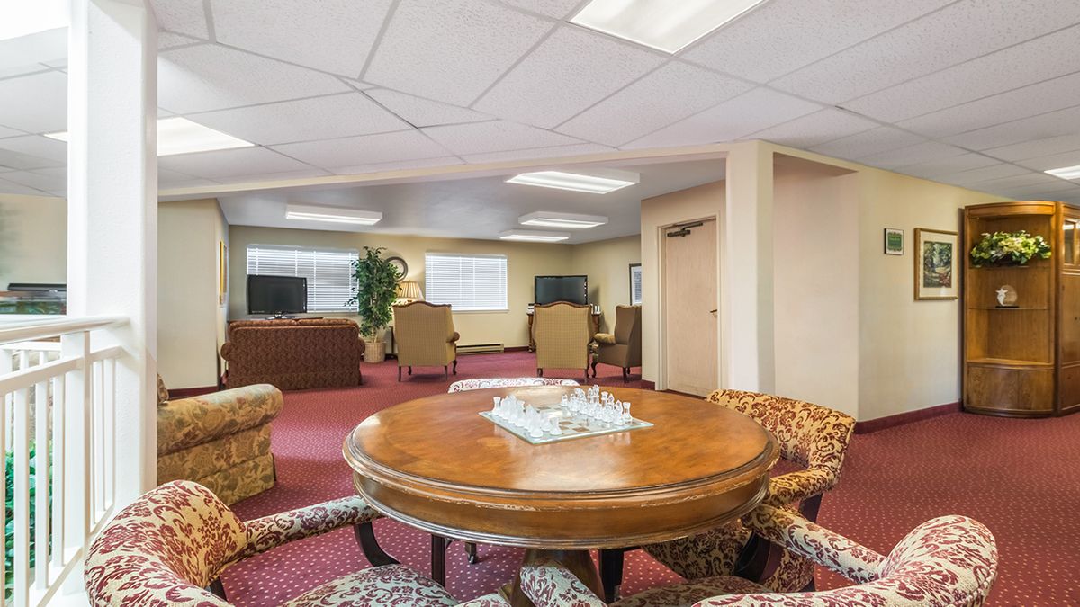 A spacious interior living room with a central round table surrounded by chairs, sofas, and a television.