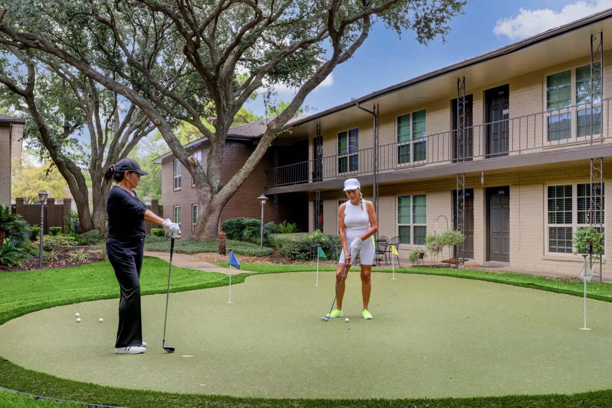 Two people playing golf on a putting green in an apartment complex.