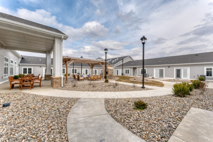 A peaceful courtyard with a central pathway, outdoor seating, and surrounding buildings under a cloudy sky.