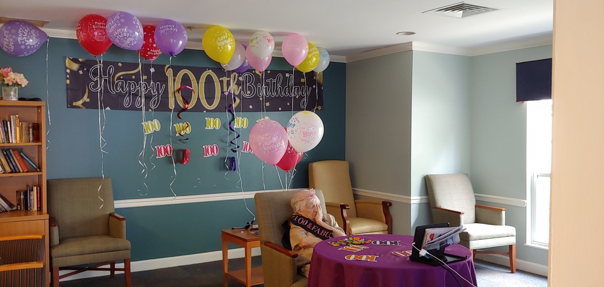 A room decorated for a birthday celebration with colorful balloons and a banner.