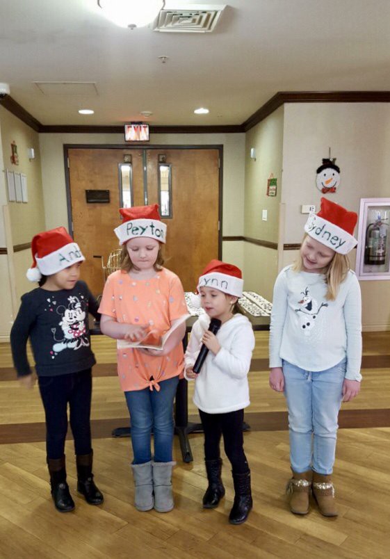 A group of children wearing Christmas hats singing together indoors.