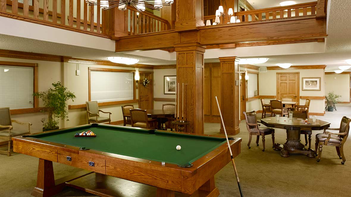 A cozy lounge area featuring a billiards table with rich wood paneling and elegant chandeliers.