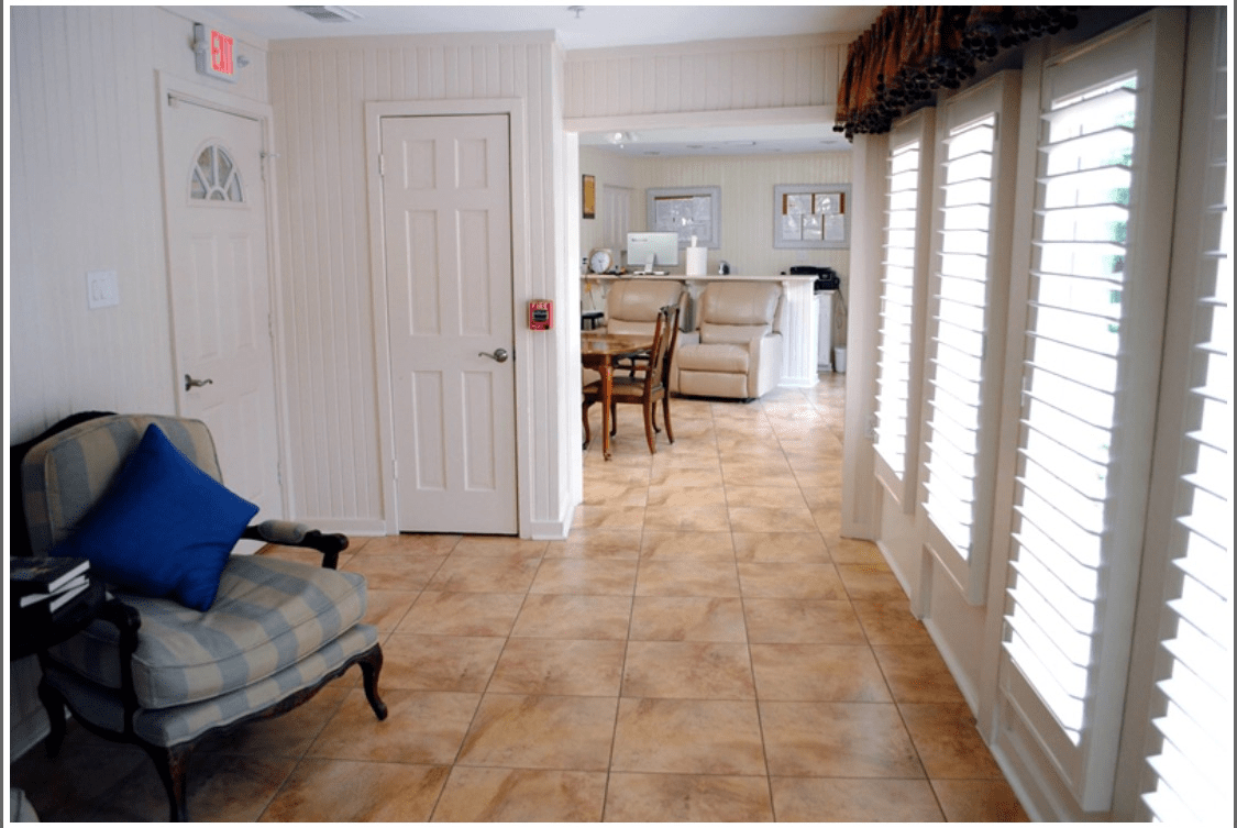 A cozy living room area with tiled floors, comfortable seating, and ample natural light from large windows.