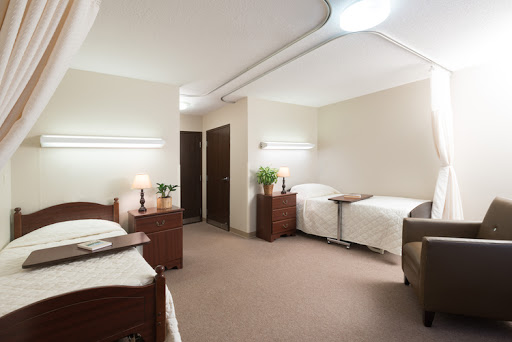 A spacious hospital room designed for patient comfort, featuring two beds and warm lighting.