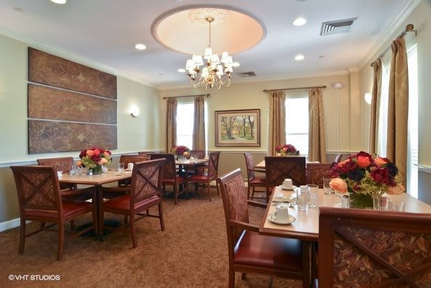 A well-decorated dining room with a chandelier, tables set for meals, and elegant decor.