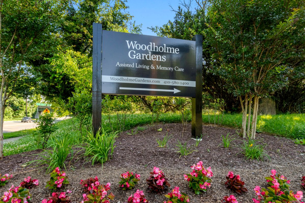 A sign at WoodBriar Gardens, surrounded by flowers and greenery.