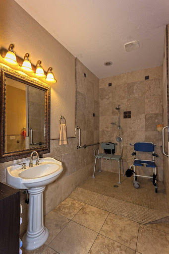 A modern, handicap-accessible bathroom featuring a sink, mirror, and shower area with tiled walls.