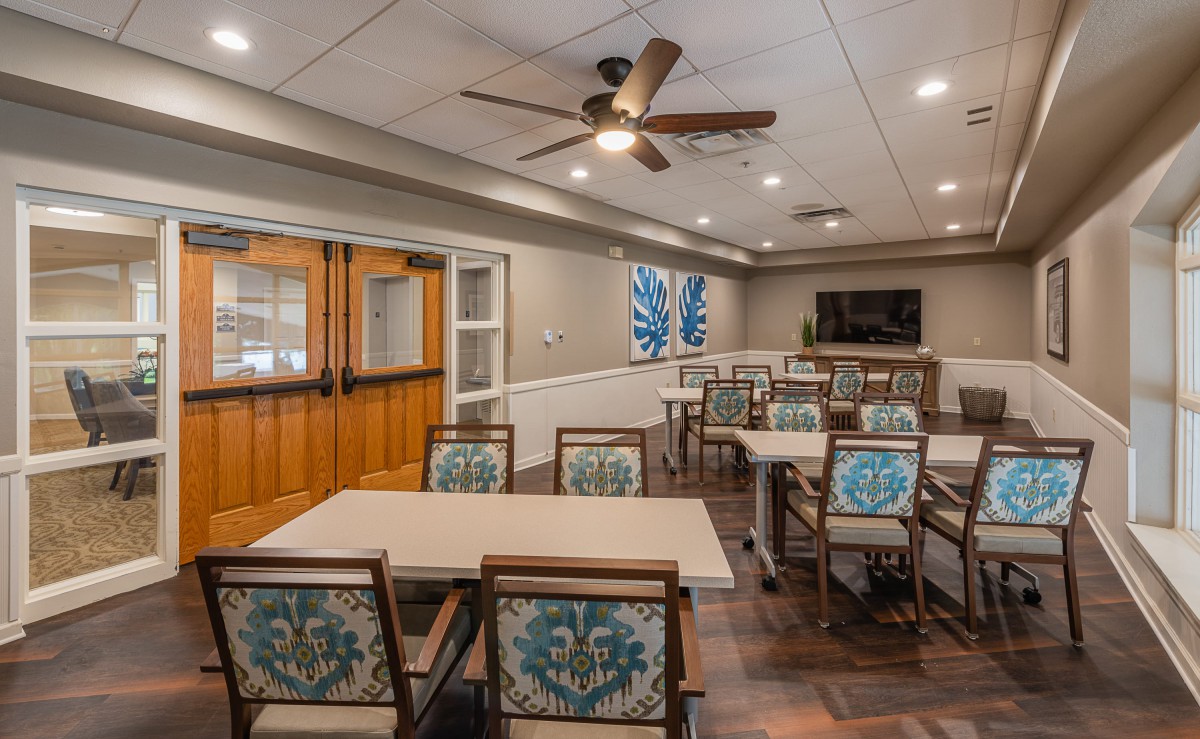 A well-appointed meeting room with tables, decorated chairs, a television, and ceiling fan.