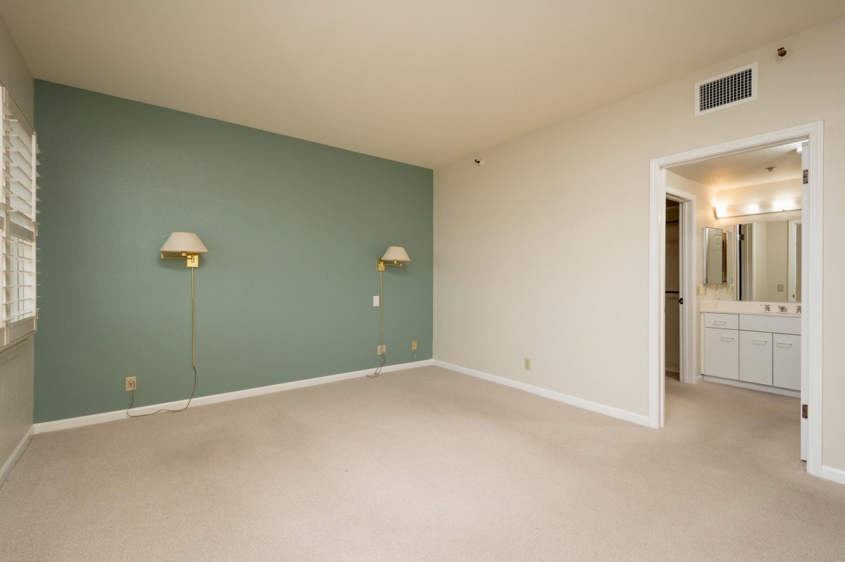 A minimalist empty room with a green accent wall, featuring wall-mounted lamps and a carpeted floor.
