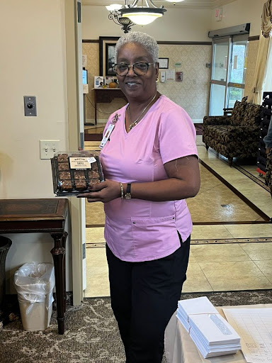 A cheerful woman in a pink shirt holding a box in a welcoming indoor environment.