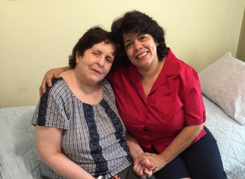 Two women sitting together and smiling indoors.