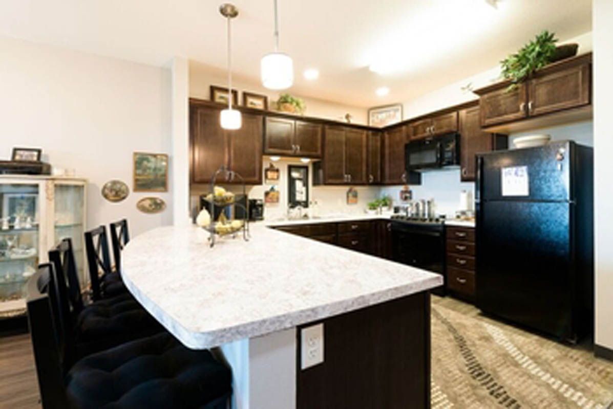 A modern kitchen with dark cabinets and a spacious white countertop, featuring pendant lighting and various appliances.