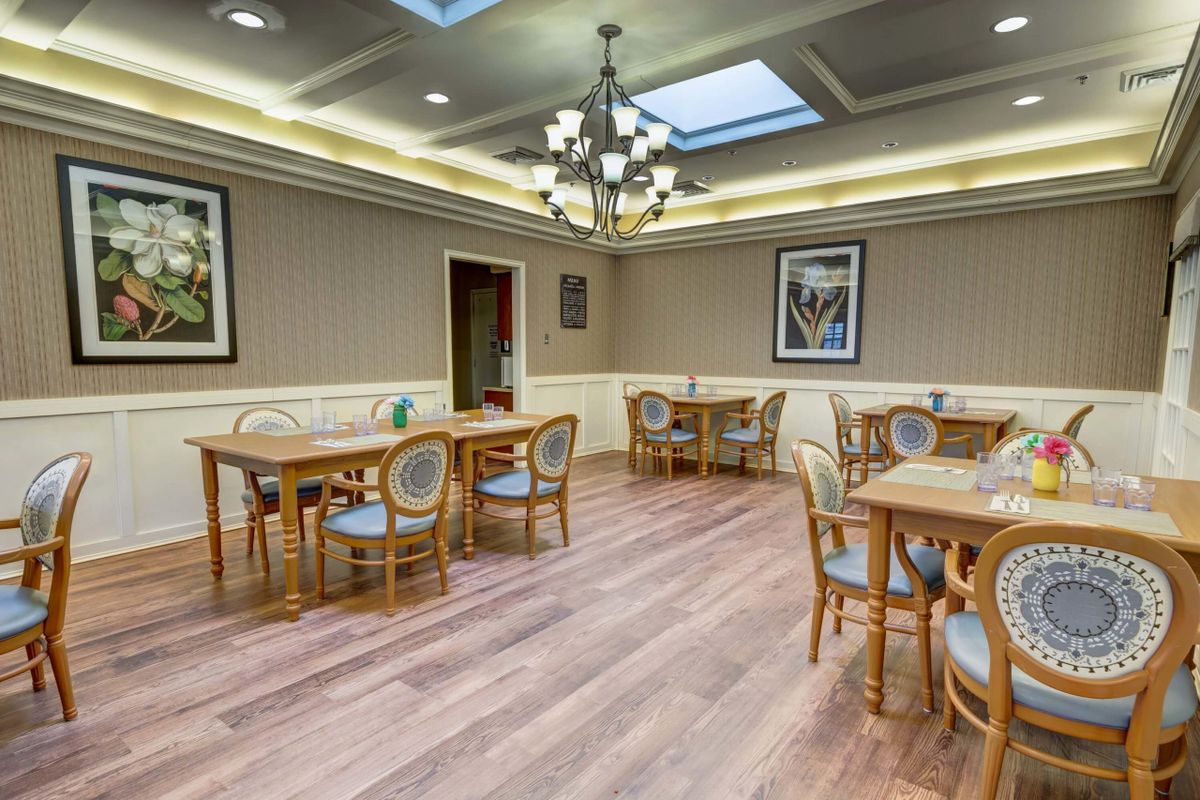 A cozy dining room with wooden tables and chairs, illuminated by a chandelier and natural light from skylights.