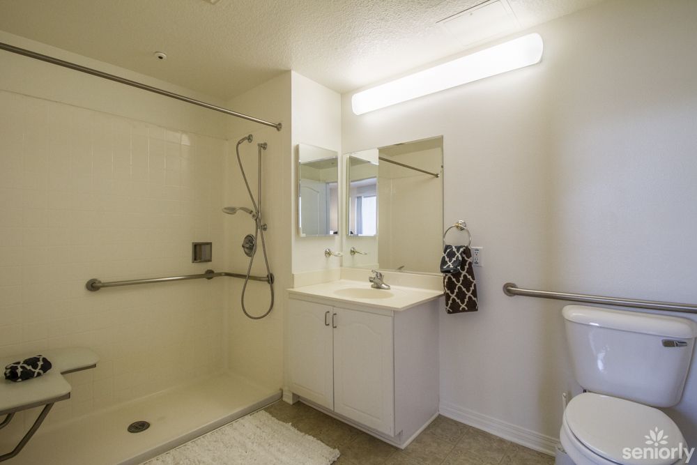 A modern, minimalist bathroom featuring a spacious shower and a sleek white vanity with a mirror.