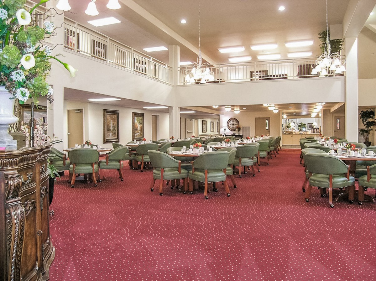 A spacious dining area with red carpet, green chairs, and ample lighting.