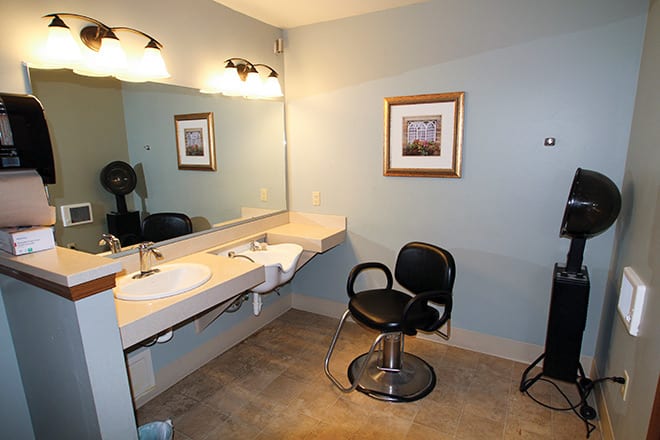 A well-lit bathroom vanity area with a mirror, chair, and sink.