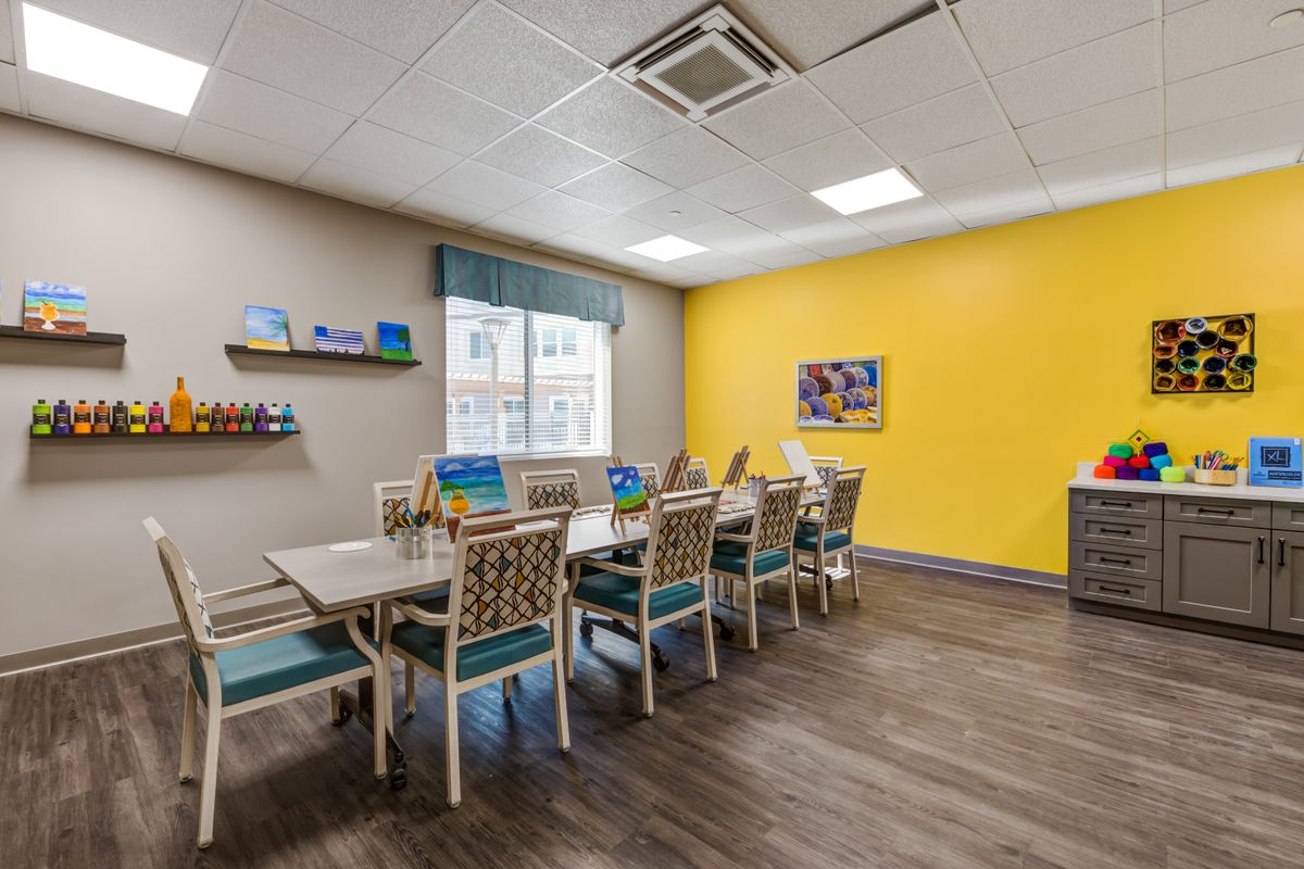 A brightly lit dining or meeting area with a yellow accent wall and neatly arranged tables and chairs.