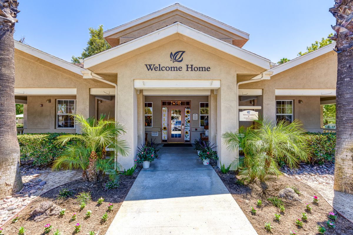 A welcoming building entrance with a 'Welcome Home' sign and surrounding palm trees.