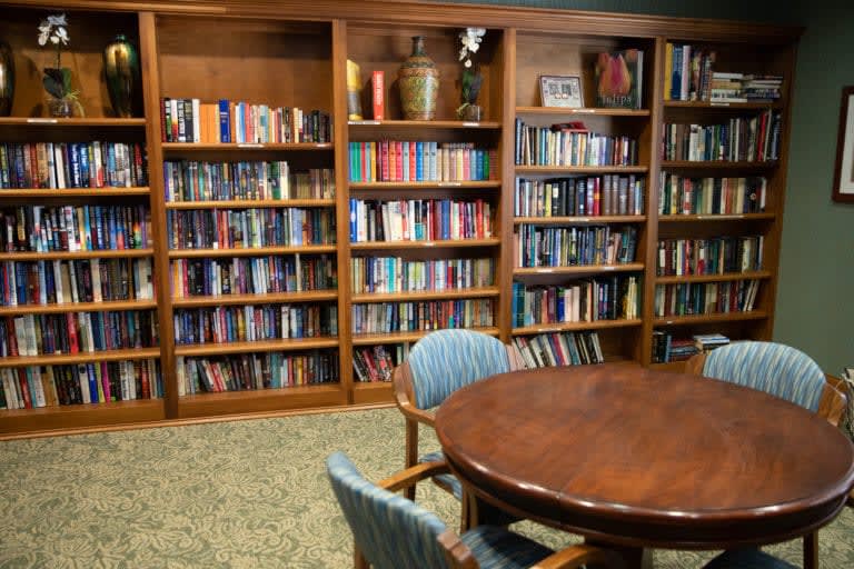 A cozy library room with wooden bookshelves filled with books and a round table surrounded by chairs.