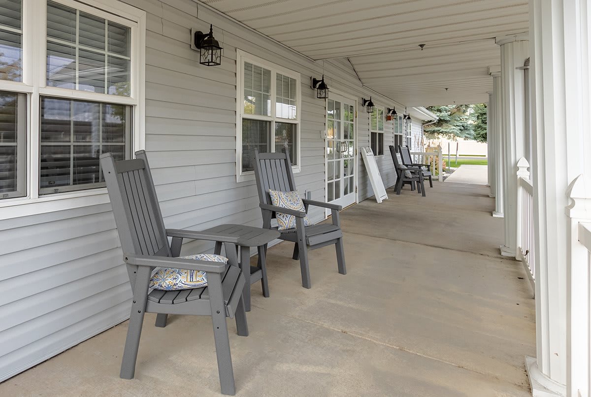 A view of an outdoor porch with several chairs lined up under a covered area.