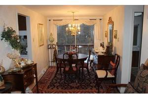A classic dining room with a dark wood table and chairs, an ornate chandelier, and decorative elements like a mirror and curtains.