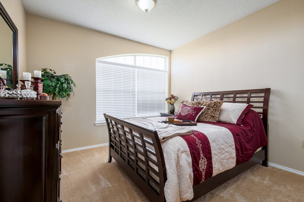 A cozy bedroom with a wooden bed frame, decorated with red and white bedding, featuring a large window and a dresser.