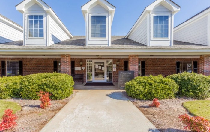 A welcoming front entrance of a brick residential building with manicured bushes and a clear pathway.