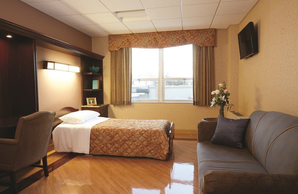 A tidy and well-lit hospital room with a single bed, sofa, and a window view.