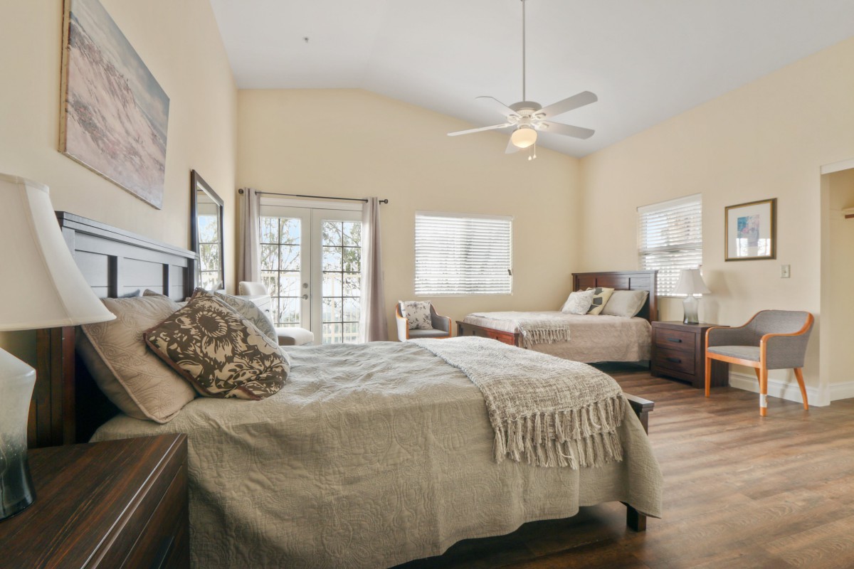 A cozy bedroom featuring two beds, natural lighting, and a ceiling fan.