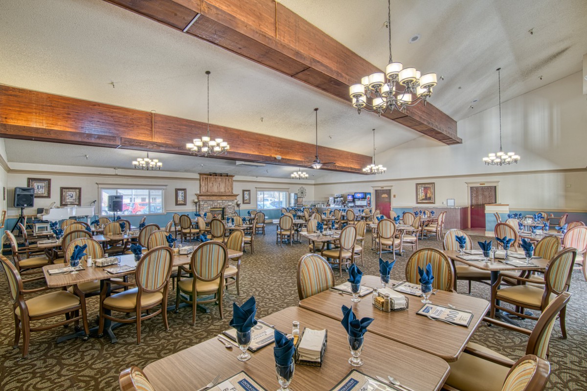 A spacious and elegantly decorated dining room with neatly arranged tables and chairs, featuring chandeliers and warm lighting.