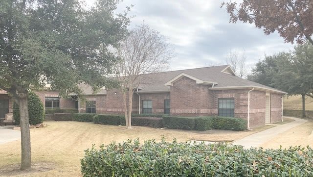 A suburban brick house surrounded by trees and bushes on a cloudy day.