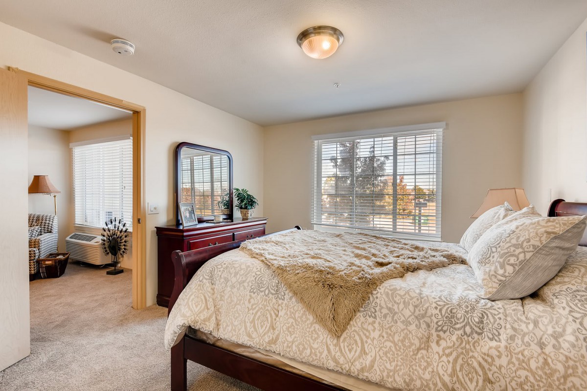 A cozy bedroom with a large bed, wooden furniture, and a window letting in natural light.