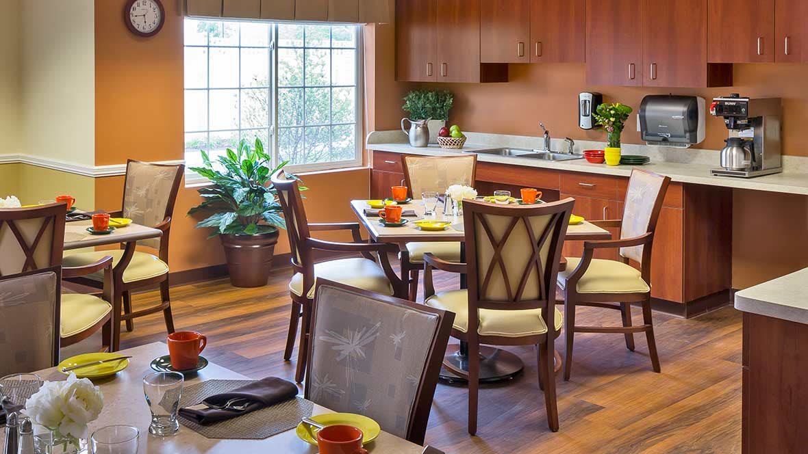 A cozy kitchen and dining area with wooden furniture and plants near a large window.
