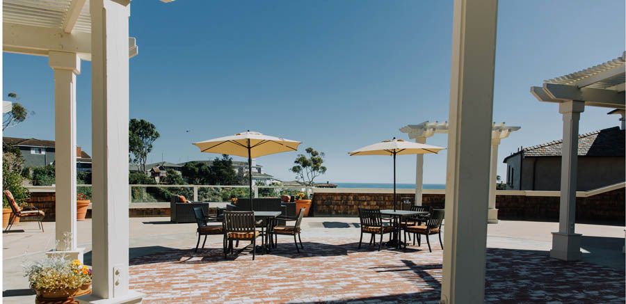 A sunny outdoor patio with tables, chairs, and umbrellas overlooking a scenic sea view.
