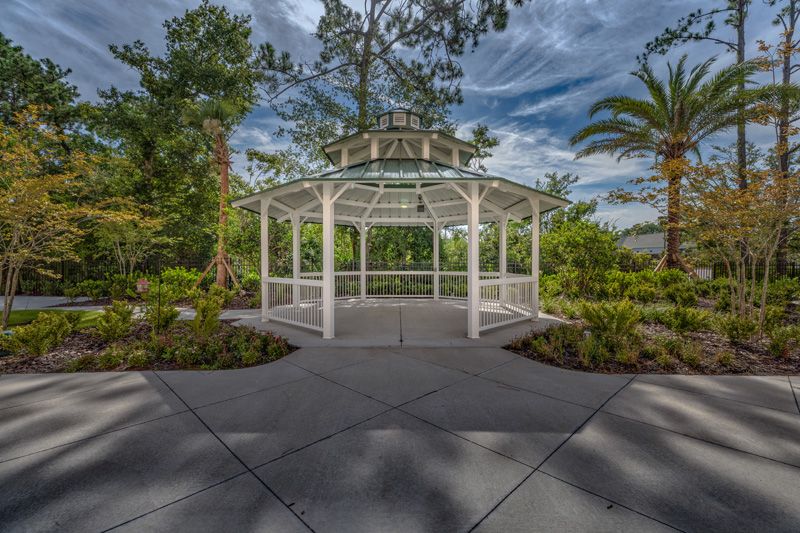 A white gazebo surrounded by lush greenery and trees under a partly cloudy sky.