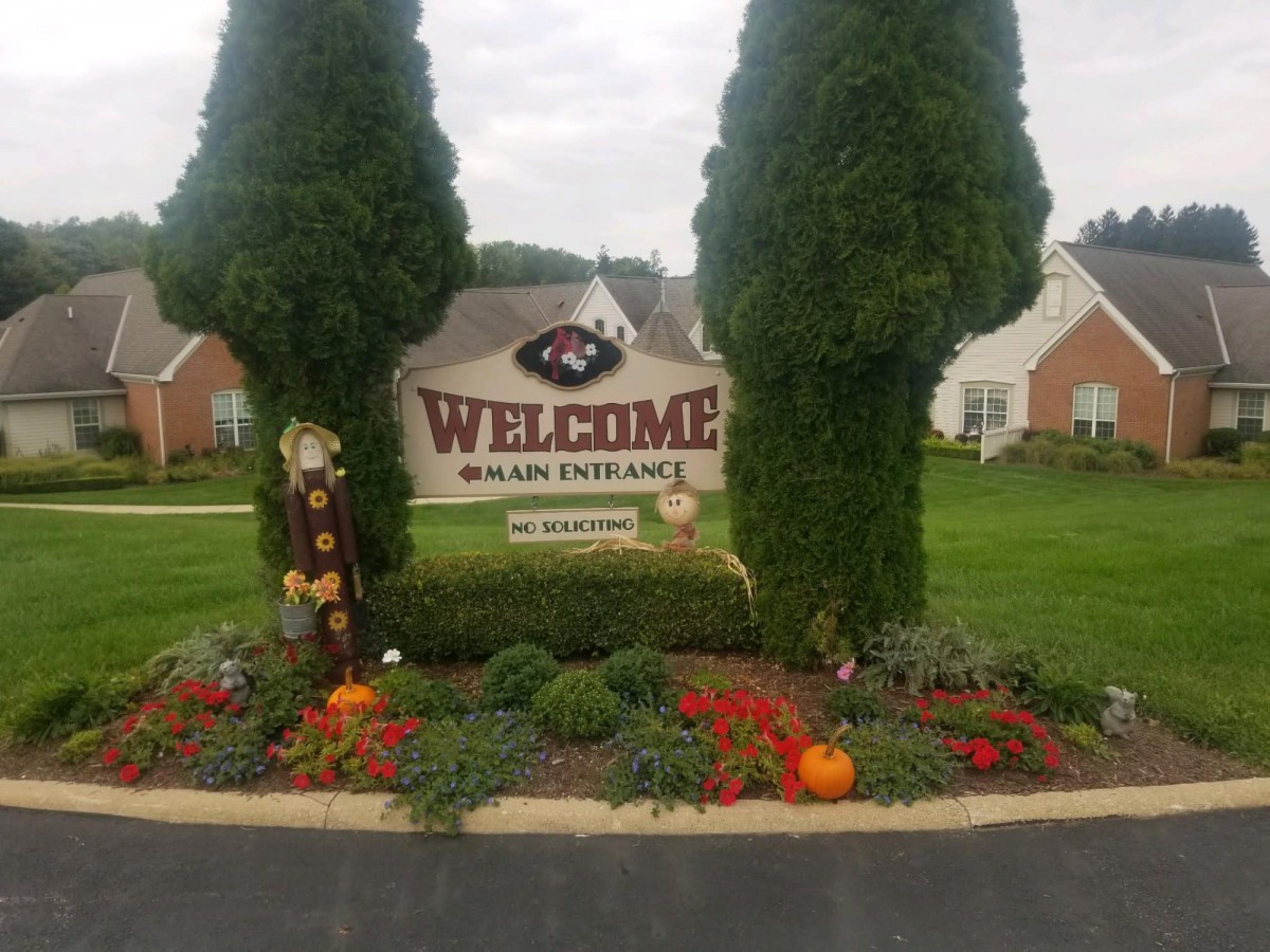 A welcoming community entrance decorated with pumpkins and a scarecrow for autumn.