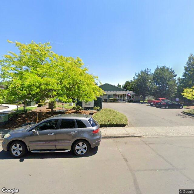 A parked car on a sunny day in front of a building and parking lot with trees.